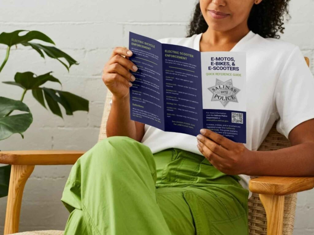 Person reading the front page of the E‑Moto, E‑Bike, E‑Scooter, and E‑Motorcycle Quick Reference Guide brochure.